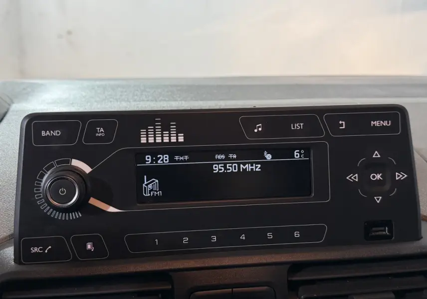 Gros plan sur l'autoradio noir du Peugeot Rifter blanc, affichant la fréquence FM 95,50 MHz et la température extérieure 6°C.
