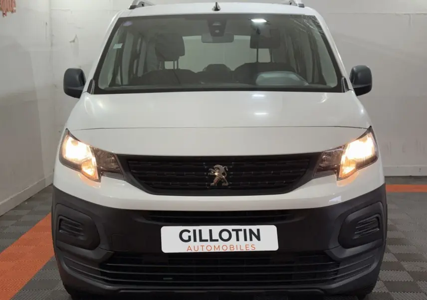 Vue frontale d'un Peugeot Rifter blanc de 2019 avec phares allumés et calandre noire distinctive.