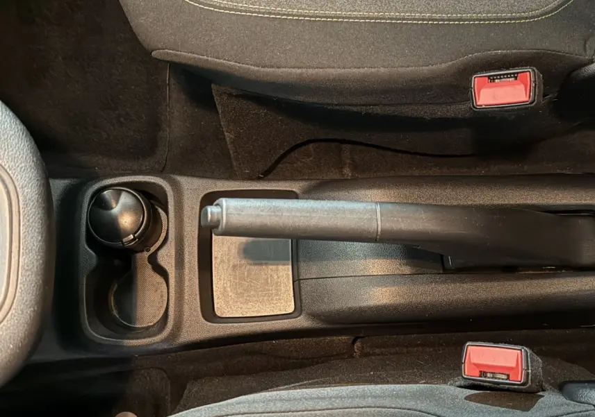 Vue rapprochée de la console centrale noire du Peugeot Rifter blanc, avec frein à main manuel et porte-gobelet.