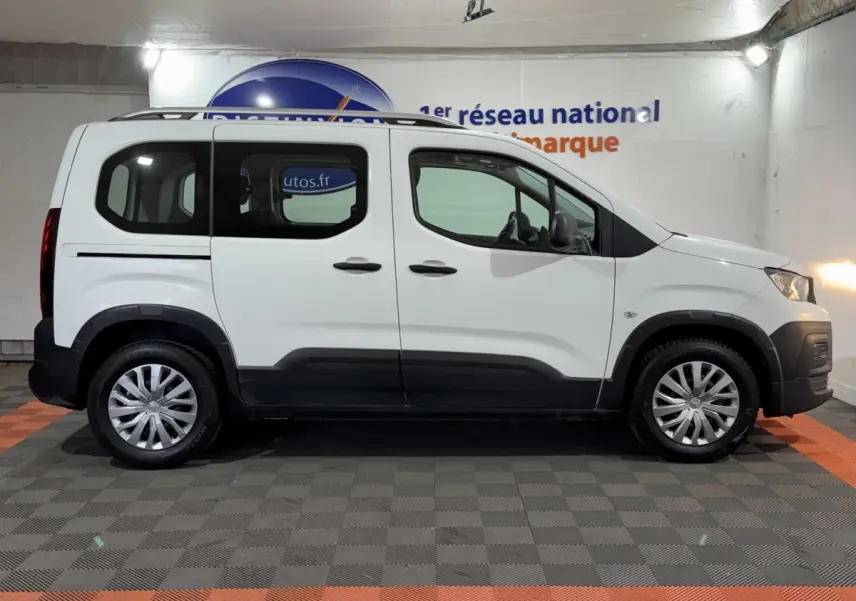 Vue de profil côté gauche d'un Peugeot Rifter blanc avec barres de toit chromées et jantes alliage.