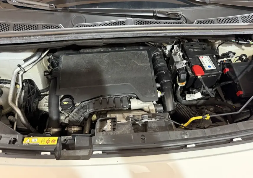 Vue plongeante sur le compartiment moteur d’un Peugeot Rifter blanc de 2019, montrant le moteur essence PureTech.