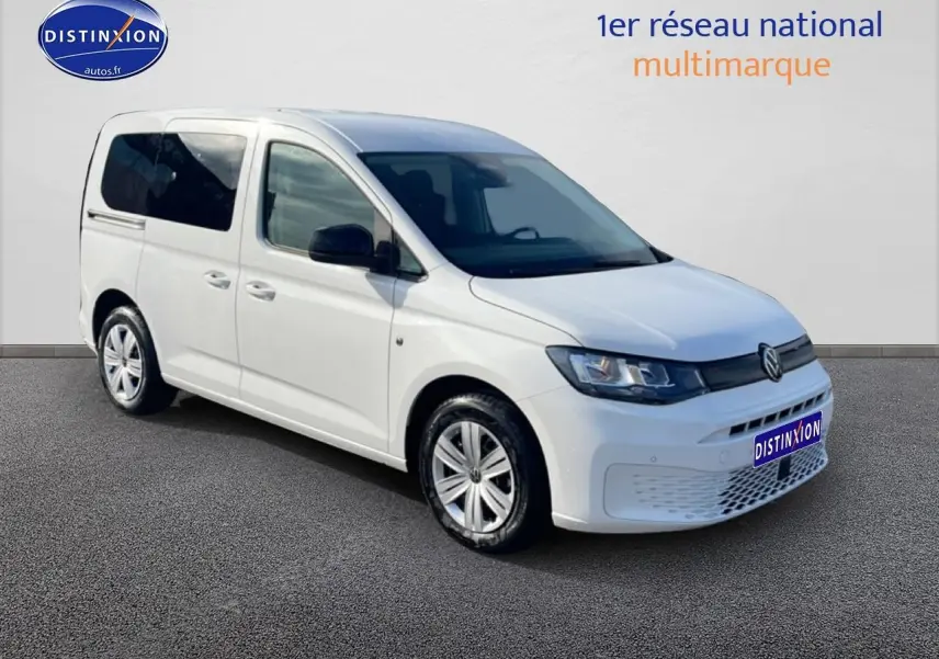 Volkswagen Caddy blanc en 3/4 avant droit, avec vitres teintées et jantes alliage visibles.
