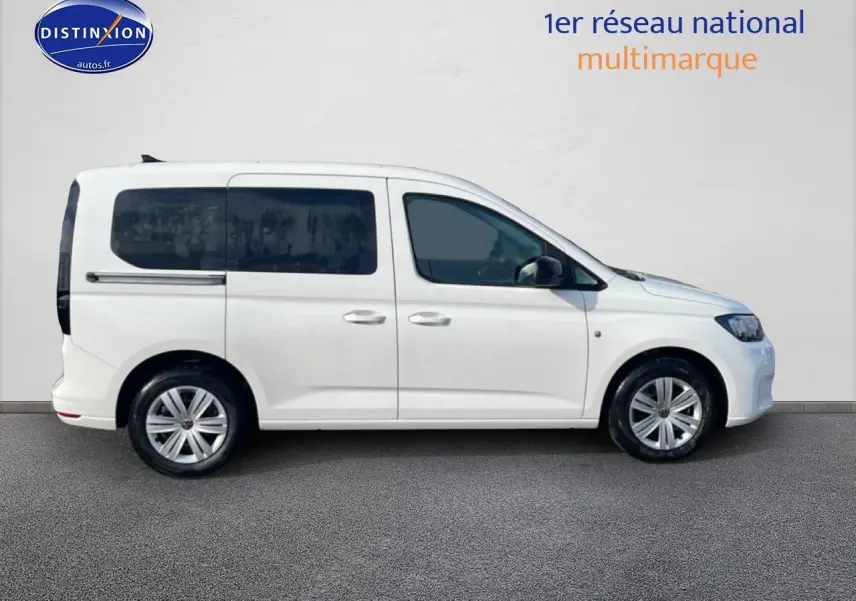 Profil droit d’un Volkswagen Caddy blanc 2025 avec vitres arrière teintées et barres de toit visibles.