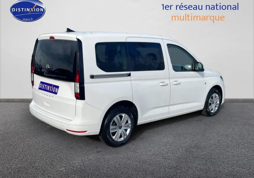 Volkswagen Caddy blanc vue 3/4 arrière droit avec vitres teintées et jantes alliage.