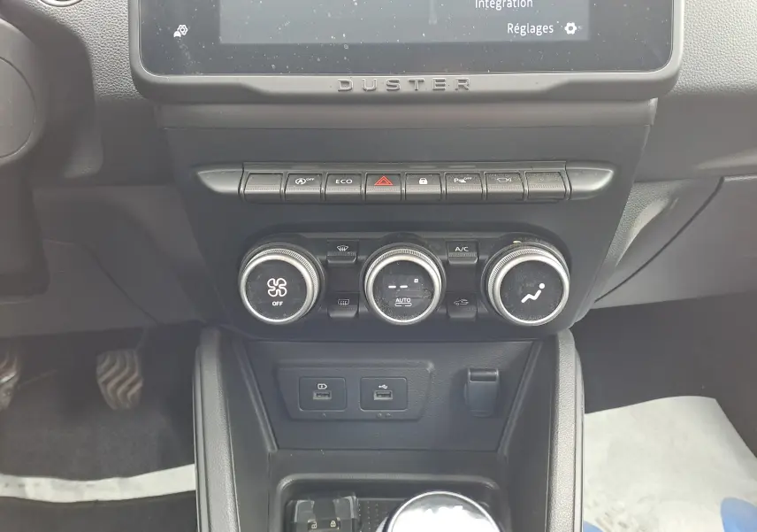 Vue rapprochée du tableau de bord central du Dacia Duster 2024, avec commandes de climatisation et écran tactile.