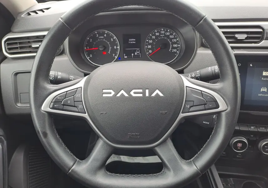 Vue rapprochée du volant noir du Dacia Duster 2024 avec tableau de bord et commandes visibles en arrière-plan.