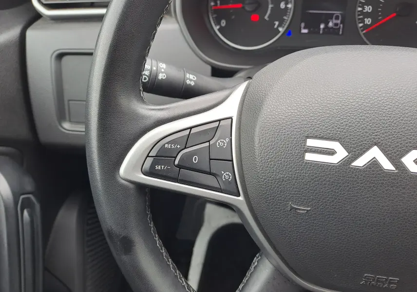 Gros plan sur le volant noir du Dacia Duster 2024, avec commandes de régulateur de vitesse visibles à gauche.