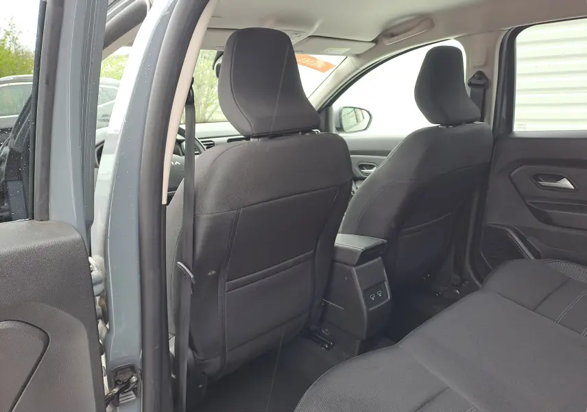 Vue intérieure arrière du Dacia Duster gris urbain 2024, montrant les sièges noirs et la console centrale avec ports USB.