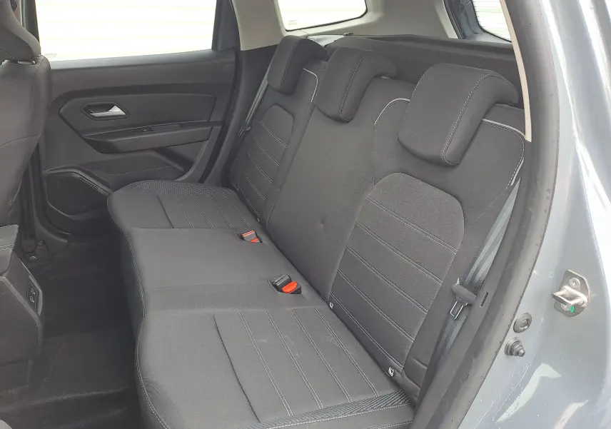 Vue intérieure côté arrière droit du Dacia Duster gris urbain 2024, montrant la banquette arrière noire avec appuie-têtes intégrés.