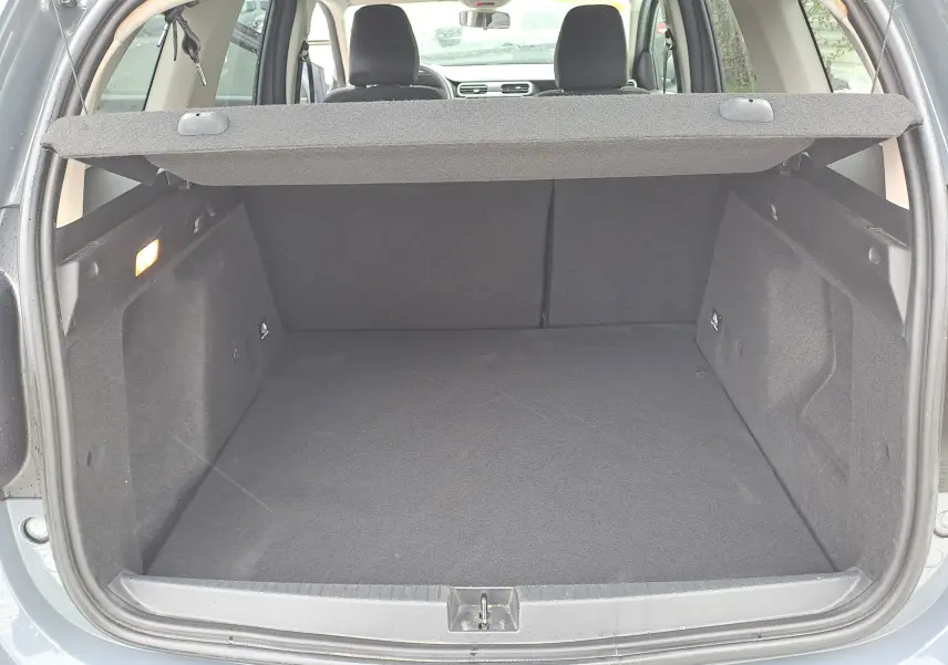 Vue du coffre ouvert d'un Dacia Duster gris urbain 2024, montrant l'espace de chargement avec cache-bagages déployé.