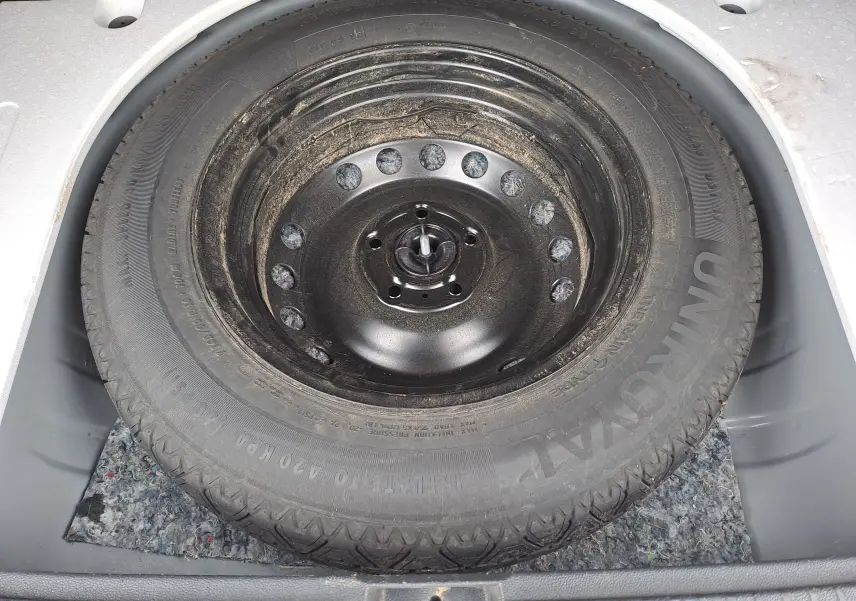 Gros plan sur la roue de secours noire et poussiéreuse dans le coffre d’un Dacia Duster gris urbain 2024.