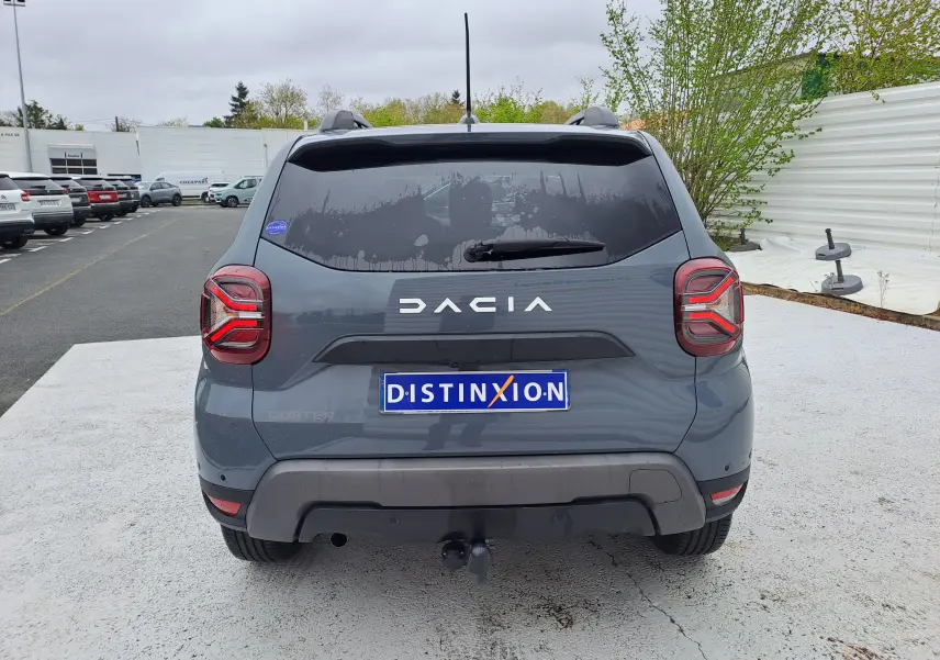 Vue arrière d’un Dacia Duster gris urbain 2024 avec feux LED et attelage visible sur un parking.