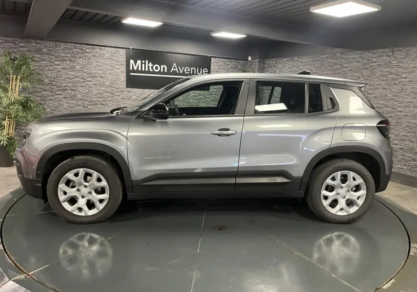 Vue de profil côté gauche d'un Jeep Avenger gris métallisé avec jantes alliage et coques de rétroviseurs noires.