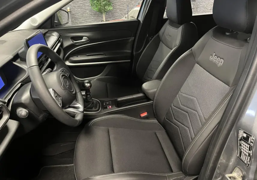 Vue intérieure côté conducteur du Jeep Avenger gris, mettant en valeur les sièges noirs avec logo Jeep brodé.