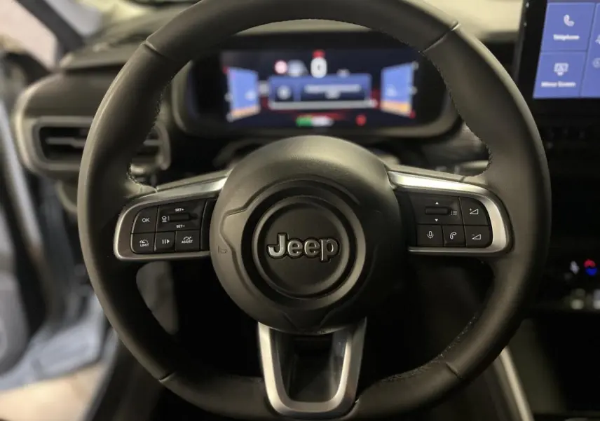 Vue rapprochée du volant en TEP noir du Jeep Avenger 2024 avec commandes intégrées et tableau de bord numérique flou.