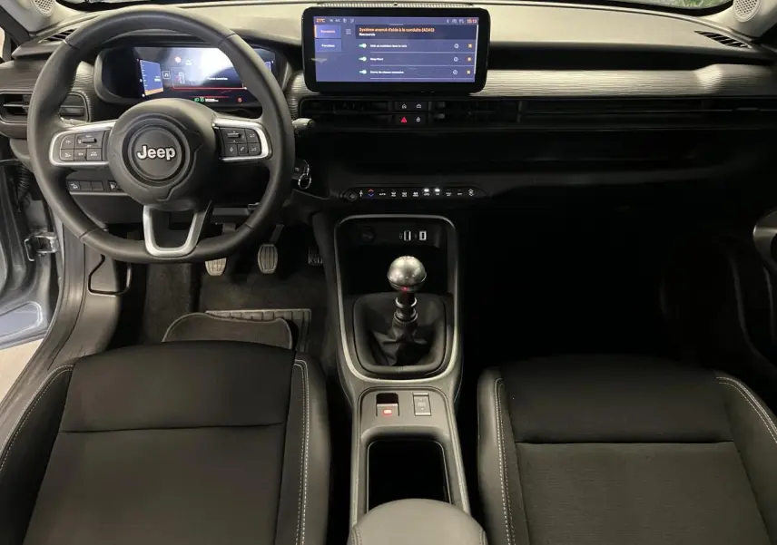 Vue intérieure frontale du tableau de bord et console centrale du Jeep Avenger 2024, volant Jeep et écran tactile visible.