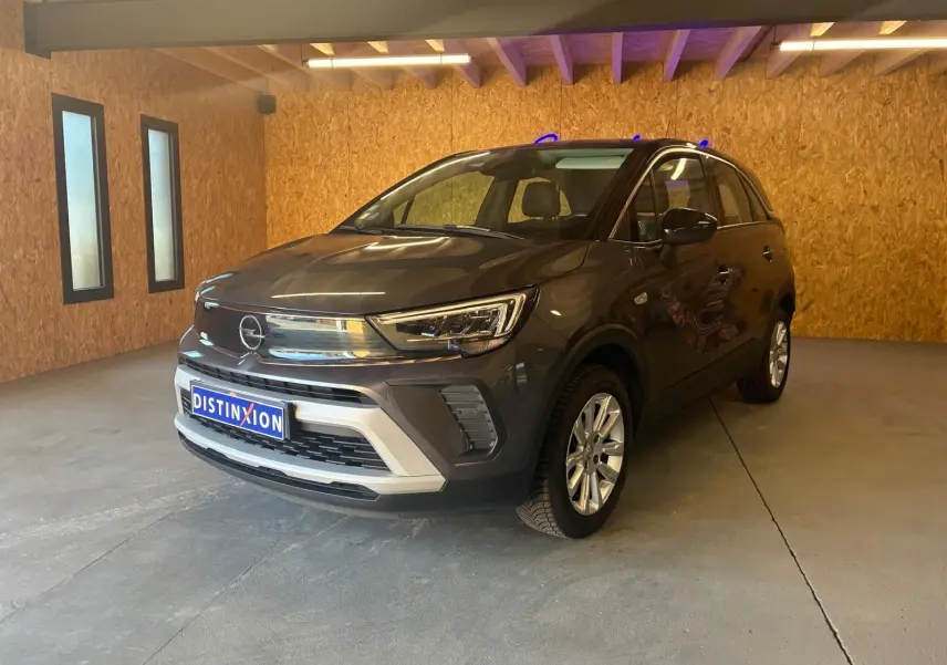 Opel Crossland gris en 3/4 avant droit, avec calandre chromée et jantes alliage dans un garage en bois.