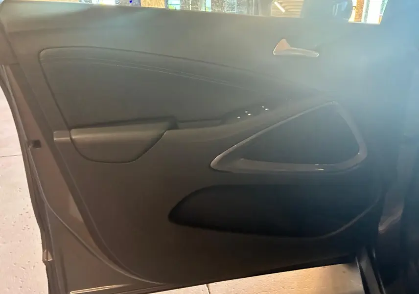 Vue intérieure de la porte côté gauche d'une Opel Crossland gris, mettant en valeur les commandes de fenêtre et la poignée argentée.