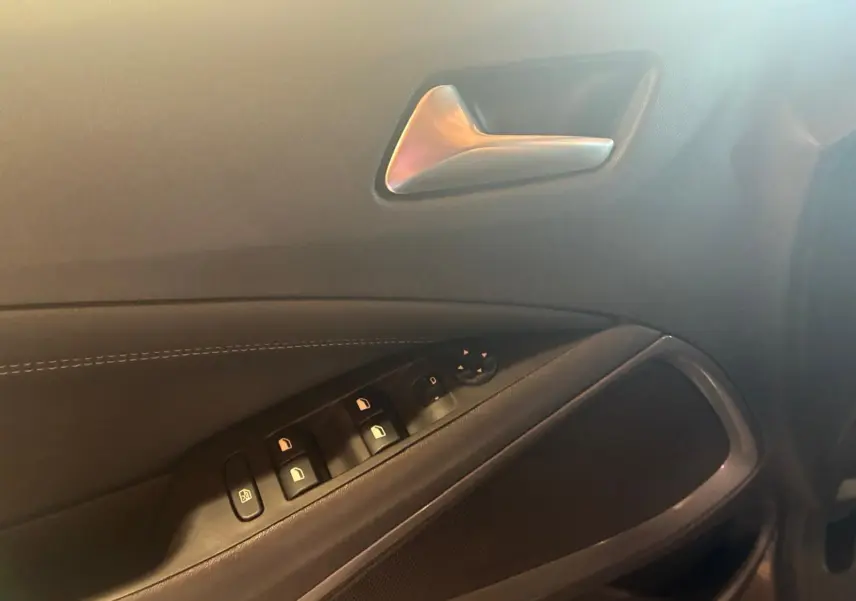 Gros plan sur la porte intérieure côté conducteur de l’Opel Crossland gris, montrant les commandes des vitres et la poignée argentée.