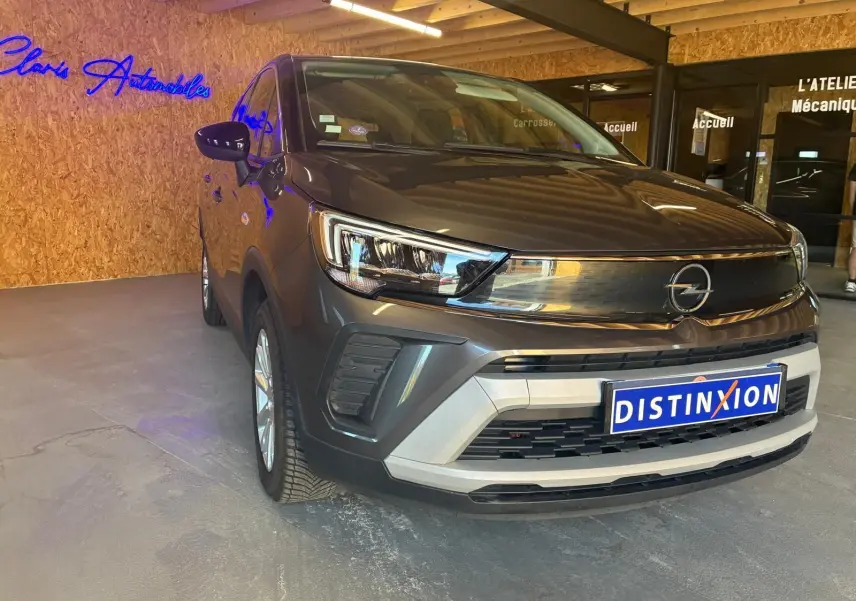 Opel Crossland gris en 3/4 avant droit, avec calandre noire brillante et plaque Distinxion visible.