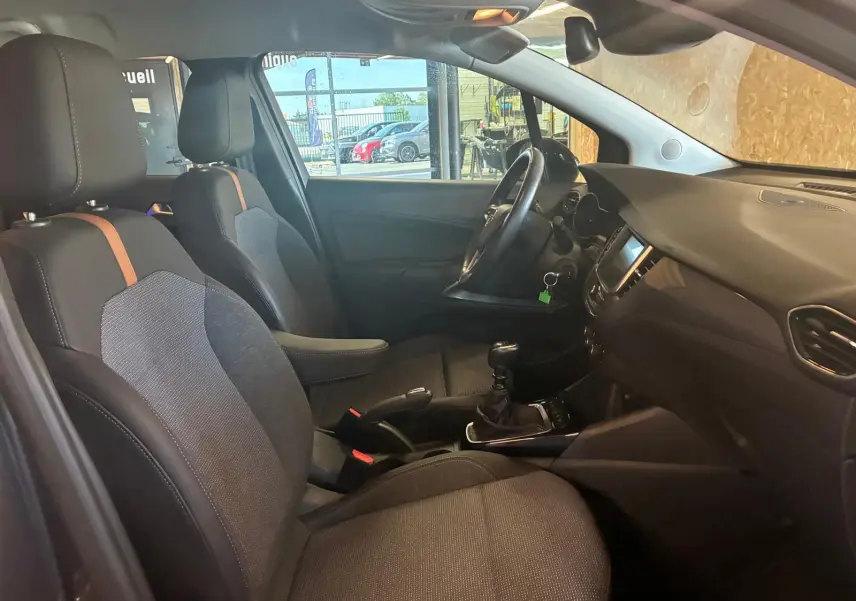 Vue intérieure côté gauche de l’Opel Crossland gris 2021, montrant les sièges tissu gris-noir et la console centrale avec boîte manuelle.
