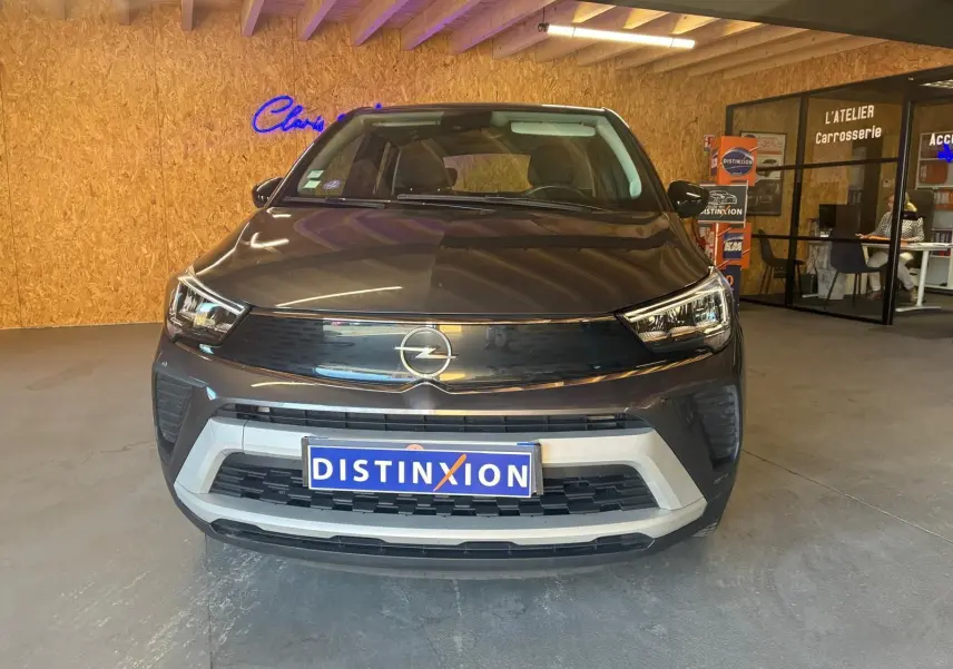 Vue frontale d’un Opel Crossland gris 2021 dans un showroom avec logo Opel et plaque Distinxion visible.