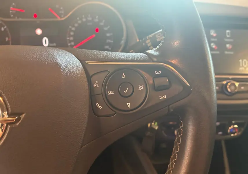 Gros plan sur les commandes au volant à droite d'un Opel Crossland gris, avec tableau de bord et écran central en arrière-plan flou.