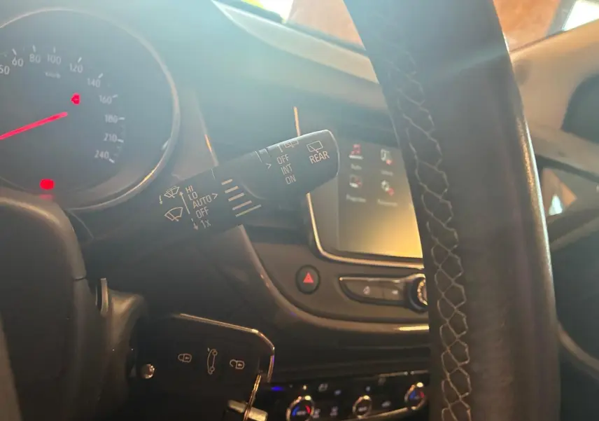 Gros plan sur la commande d’essuie-glace à gauche du volant d’un Opel Crossland gris, tableau de bord et écran tactile en arrière-plan.