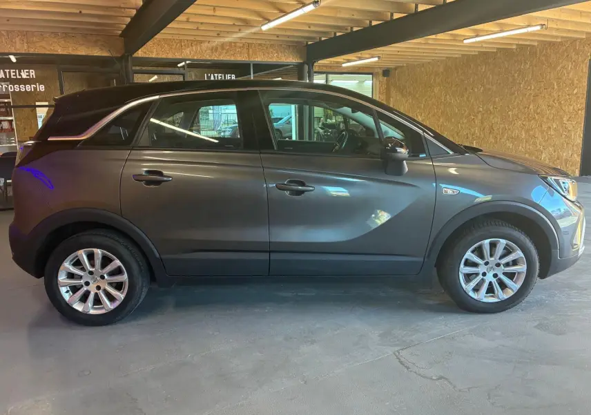 Vue de profil côté gauche d’un Opel Crossland gris 2021 avec jantes alliage et toit noir dans un garage.