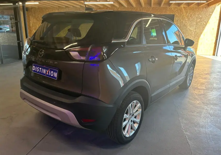Vue 3/4 arrière droite d'un Opel Crossland gris 2021 avec jantes alliage et hayon fermé dans un garage.