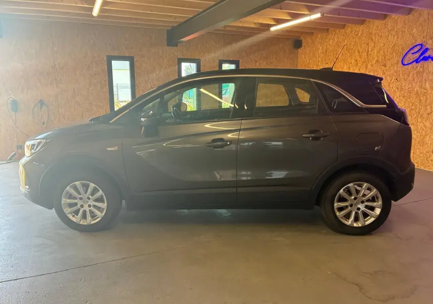 Vue de profil côté gauche d'un Opel Crossland gris 2021, version 1.2 Turbo 110 Elegance, en intérieur.