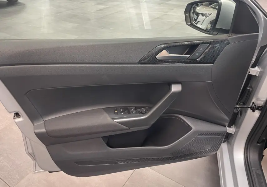 Vue de la porte avant droite ouverte d’une Volkswagen Polo gris clair, avec commandes électriques et insert décoratif noir.