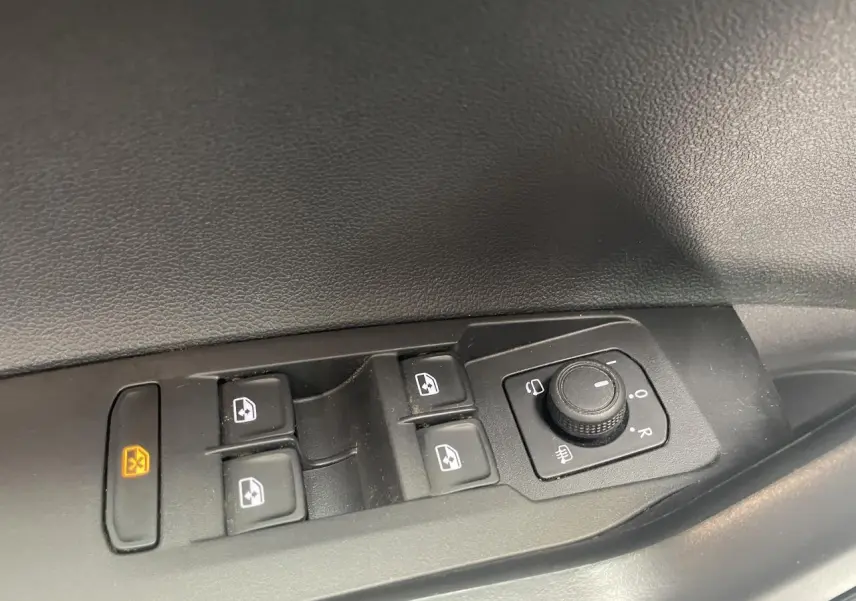 Gros plan sur les commandes de lève-vitres et réglage des rétroviseurs côté conducteur d’une Volkswagen Polo gris clair.