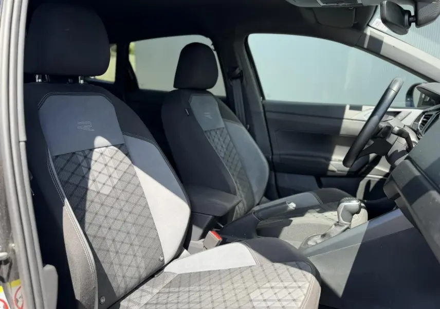 Vue intérieure côté gauche du Volkswagen Taigo TSI 116 DSG R-Line 2025, sièges sport tissu gris avec logo R-Line.