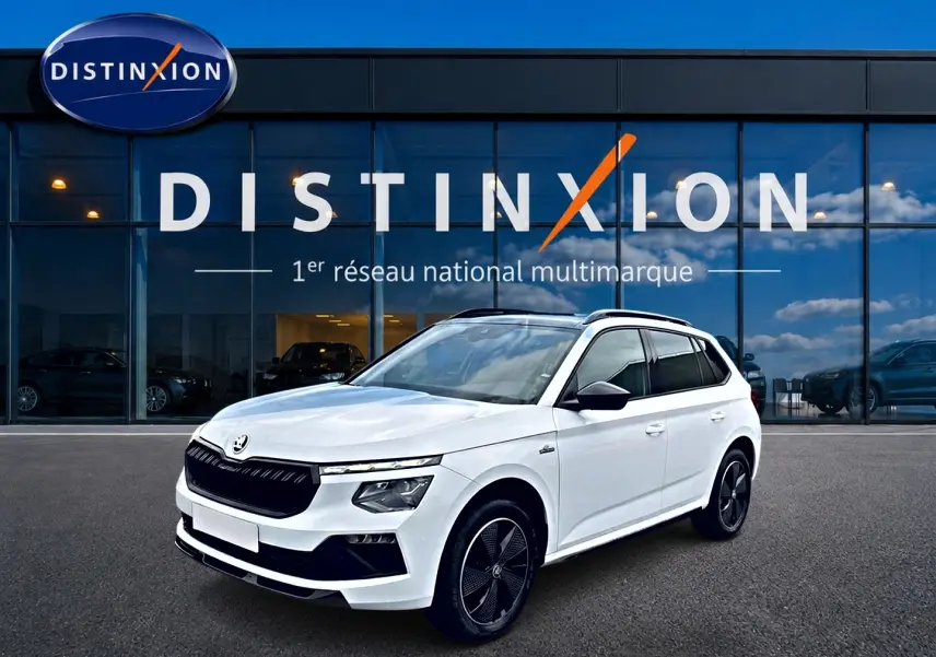 SKODA KAMIQ blanc nacré en 3/4 avant, avec jantes noires et toit panoramique visible devant une vitrine Distinxion.
