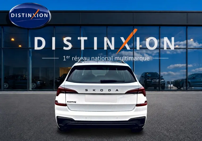 Vue arrière d'un Skoda Kamiq blanc nacré avec logo distinctif, garé devant une vitrine Distinxion.