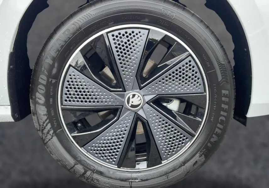 Gros plan sur la jante noire et grise à motifs perforés d’un SKODA KAMIQ blanc nacré, roue avant droite.
