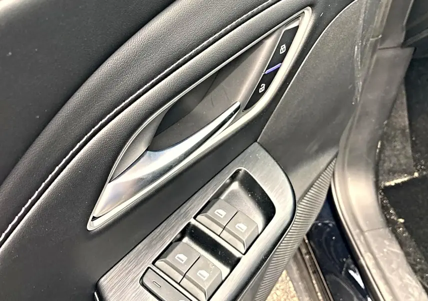 Détail de la porte avant gauche du MG ZS noir, avec commandes électriques des vitres et poignée argentée.