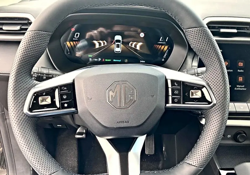 Vue rapprochée du volant noir perforé MG ZS 1.5 hybrid 197 luxury avec tableau de bord numérique en arrière-plan.