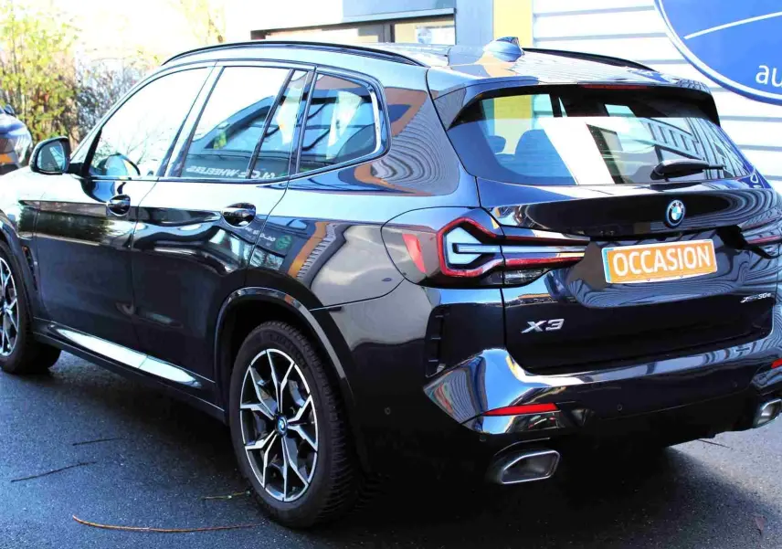 Vue 3/4 arrière côté gauche d'un BMW X3 xDrive 30e 2023 bleu métal avec jantes M Sport et badge hybride rechargeable.