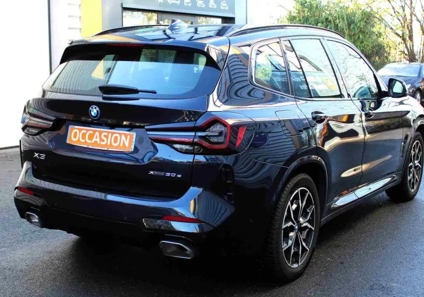 Vue 3/4 arrière droite d'un BMW X3 xDrive 30e hybride rechargeable bleu métal avec jantes M Sport en 2023.