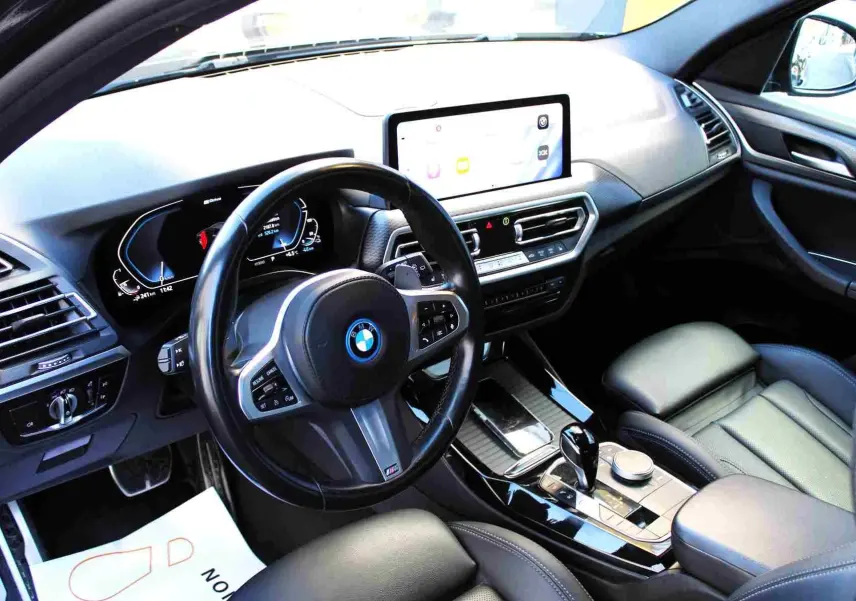 Intérieur du BMW X3 xDrive 30e 2023 vu côté conducteur, avec tableau de bord numérique et console centrale noire brillante.