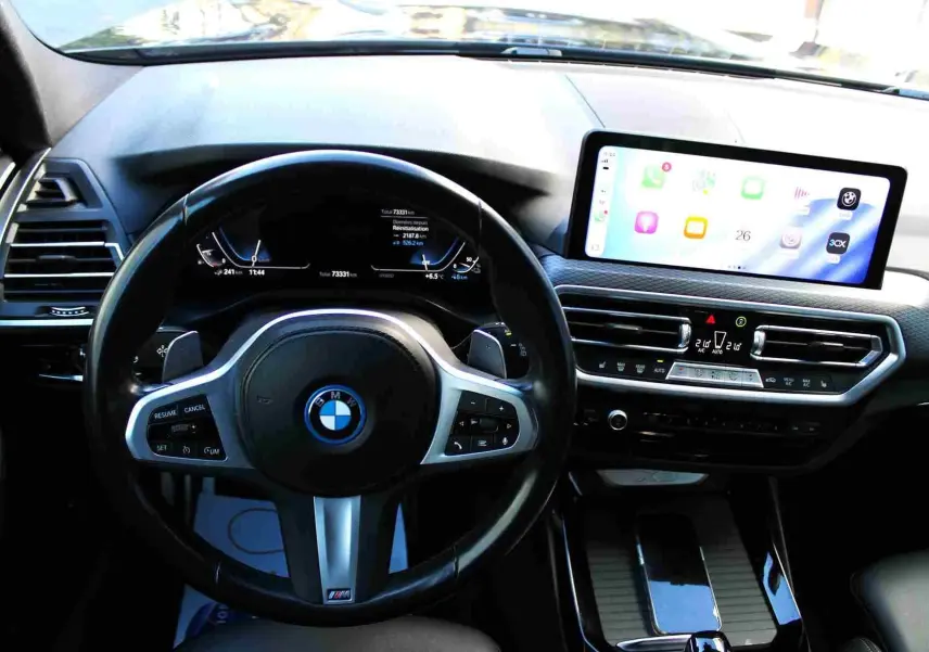 Vue intérieure du tableau de bord du BMW X3 xDrive 30e 2023, avec volant M Sport et écran tactile central lumineux.