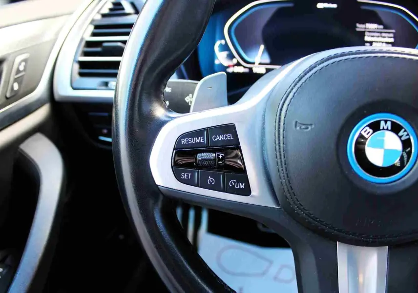 Gros plan sur le volant cuir noir avec commandes de régulateur sur la BMW X3 xDrive hybride rechargeable 2023.