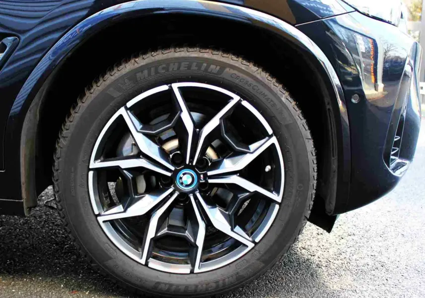 Gros plan sur la roue avant gauche du BMW X3 xDrive 30e 2023 bleu métal avec jante alliage au design sportif.