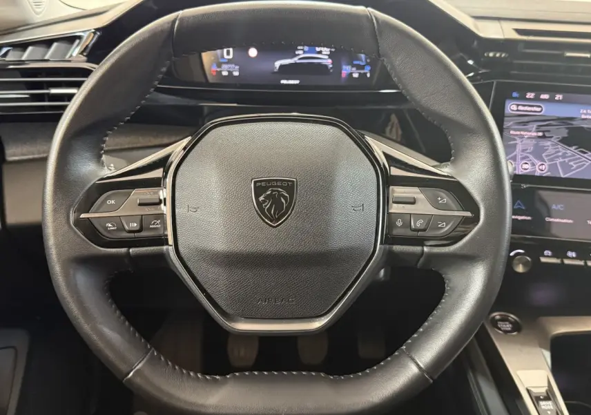 Vue rapprochée du volant cuir noir de la Peugeot 308 2023 avec commandes multifonctions et tableau de bord numérique.