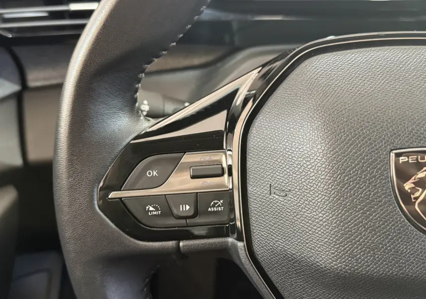 Gros plan sur le volant cuir noir de la Peugeot 308 2023, avec commandes multifonctions et logo lion central.