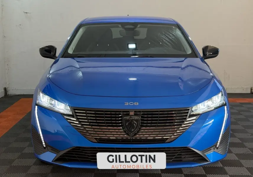 Vue frontale d'une Peugeot 308 bleu vif avec calandre noire et phares LED allumés dans un garage.