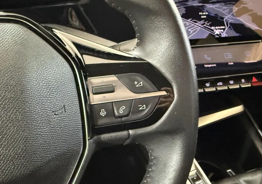 Gros plan sur le volant cuir noir de la Peugeot 308 2023, avec commandes vocales et téléphone visibles.