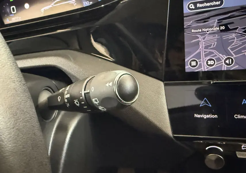 Gros plan sur la commande d’essuie-glace et partie du tableau de bord noir avec écran tactile affichant la navigation dans une Peugeot 308 bleu.
